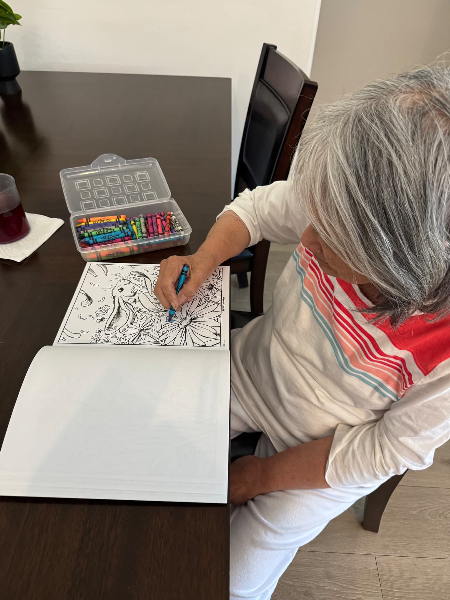 A resident coloring a flower page at the dining table with crayons